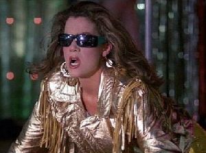 Claudia Christian : still from a movie wearing black sunglasses and a shiny old-fashioned golden jacket