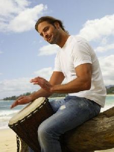 Josh Holloway : sitting on a tree trunk playing the drum