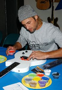 Josh Holloway : coloring a guitar with his fingers at a Guitar Charity Event