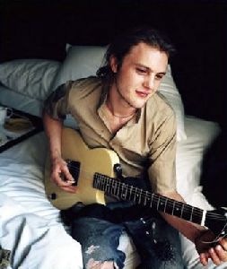 Michael Pitt wearing a torn jeans pants and playing an electric guitar