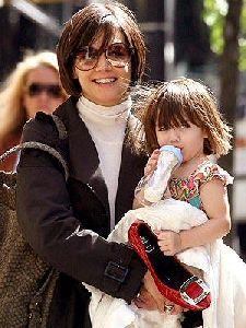 Suri Cruise drinking a bottle of milk.. Notice the red shoe she is carrying in her left hand