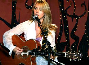 Liz Phair singing on stage and playing an accoustic guitar