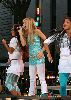 Miley Cyrus performs on stage as Hannah Montana wearing a glittery blue top and white pants