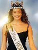 Azra Akin walking on stage in a black dress and the miss world crown