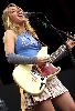 Liz Phair playing an electric guitar live wearing gray sleeves and a sport-looking blue top